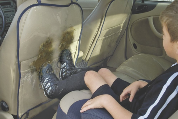 A young boy sitting in a car's back seat after soccer, making muddy shoe marks on the clear plastic front seat protector.