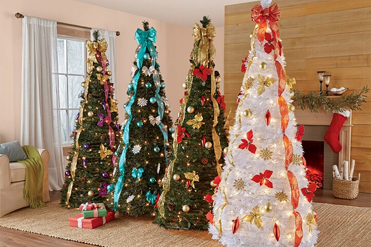 Four decorated Christmas trees in a cozy living room, featuring colorful ornaments and ribbons, with gifts underneath.