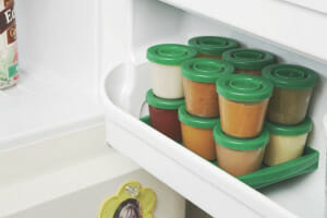Homemade baby food in a set of jars with matching green lids, stacked in the shelf of a refrigerator door.