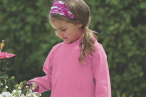A young girl outside touching flowers in a planter, wearing a pink long sleeve hoodie for sun protection.