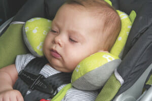 A sleeping baby safely strapped in an infant car seat, with his head extra snug in a padded head protector.