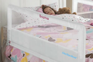 A personalized fabric and mesh side guard rail for a twin size bed protects a sleeping girl under her pink butterfly bedding.