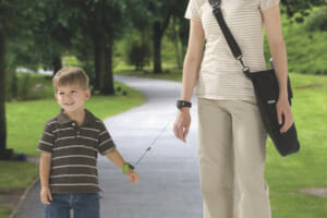 A woman and a young boy going for a walk in the park, with the boy's wrist tethered to the woman's wrist for safety.