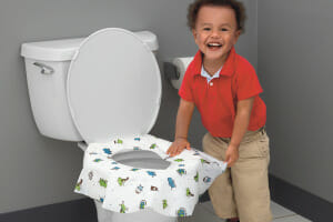A toddler boy in a red shirt in front of a toilet covered with a washable potty protector.