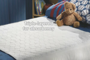 A twin size bed with a navy blue bed set that has been protected from bedwetting with a white waterproof mattress pad.