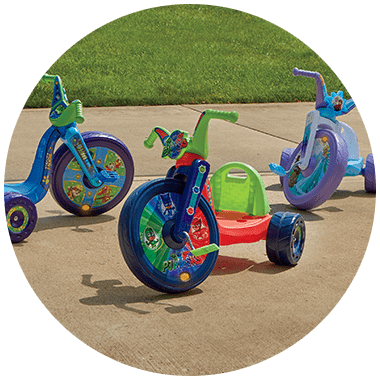 Three different Kids' big front wheel bikes outside on a driveway, with green grass in the background.